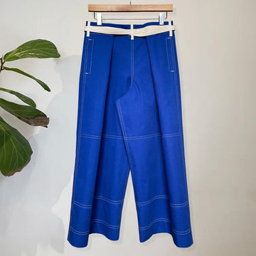 Blue trousers with white stitching on a hanger against a white background