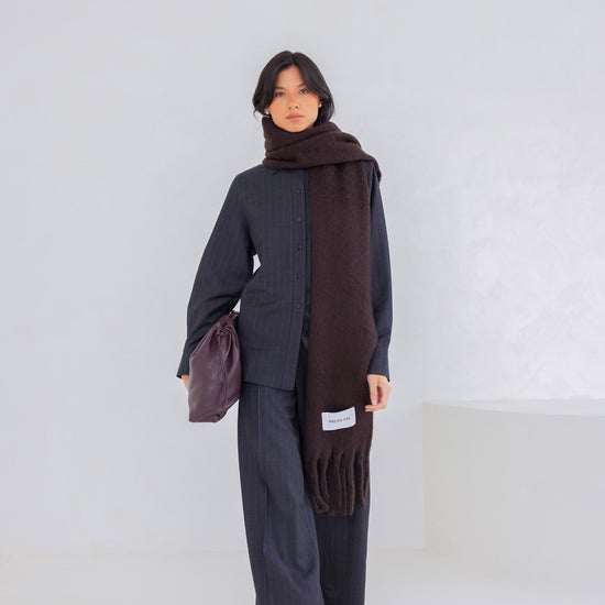 Person wearing a dark outfit with a brown scarf against a white background