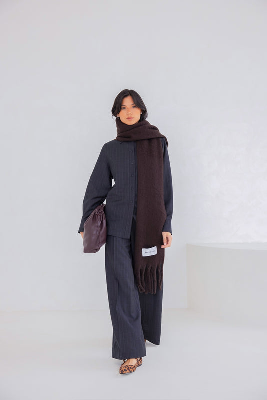 Person wearing a dark outfit with a brown scarf against a white background