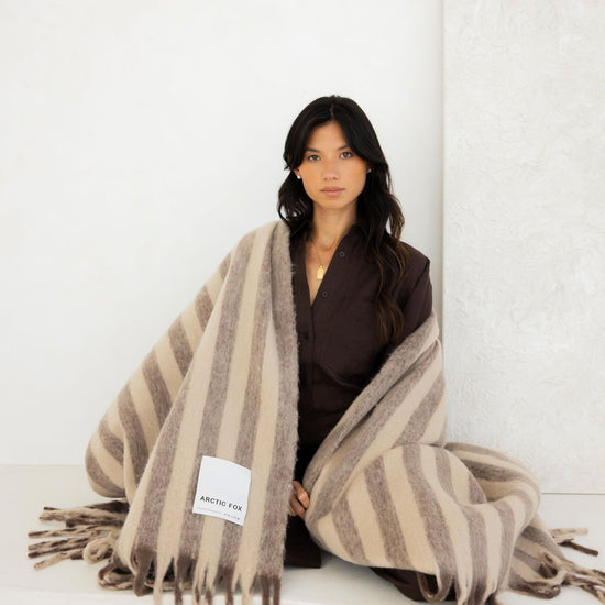 Woman wrapped in a striped blanket with a visible brand label on a white background