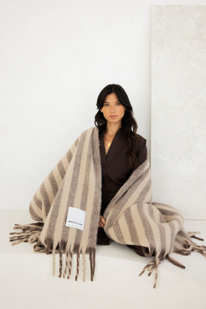 Woman wrapped in a striped blanket with a visible brand label on a white background
