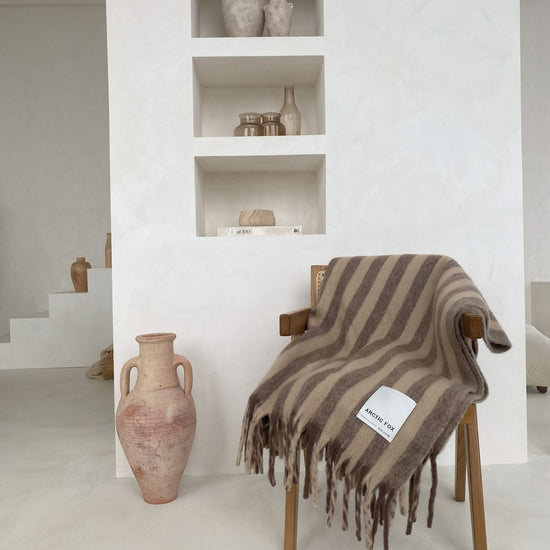 Striped blanket draped over a chair next to decorative vases in a minimalistic room.