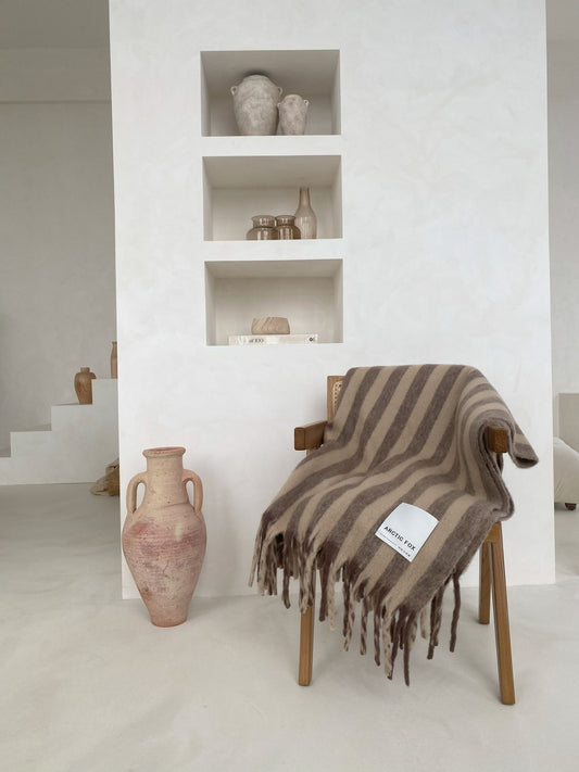 Striped blanket draped over a chair next to decorative vases in a minimalistic room.