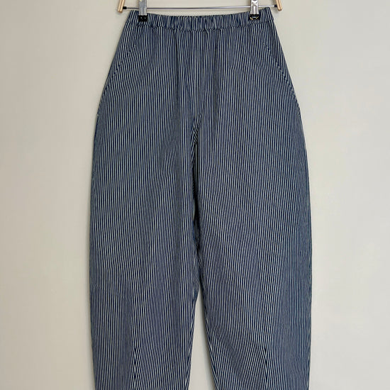 Blue and white striped barrel leg trousers hanging on a wooden hanger against a light gray background