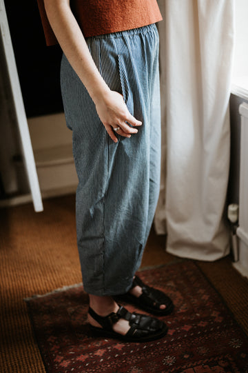 Person wearing blue striped denim trousers and sandals indoors.
