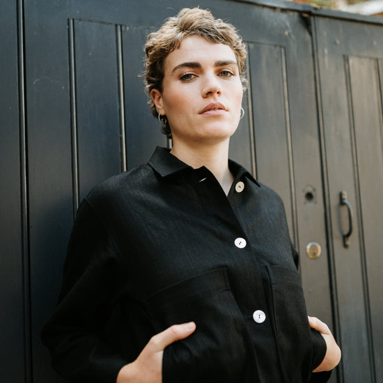 Woman wearing a black coat with white buttons against a black metal gate.