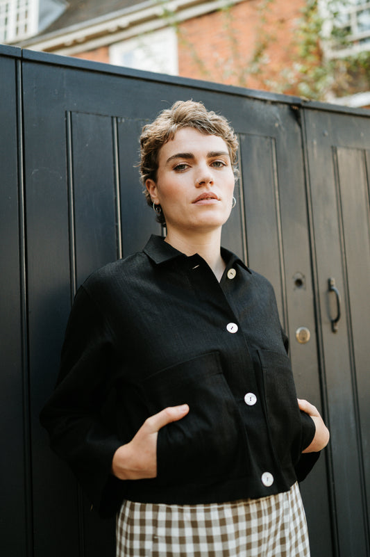 Woman wearing a black coat with white buttons against a black metal gate.