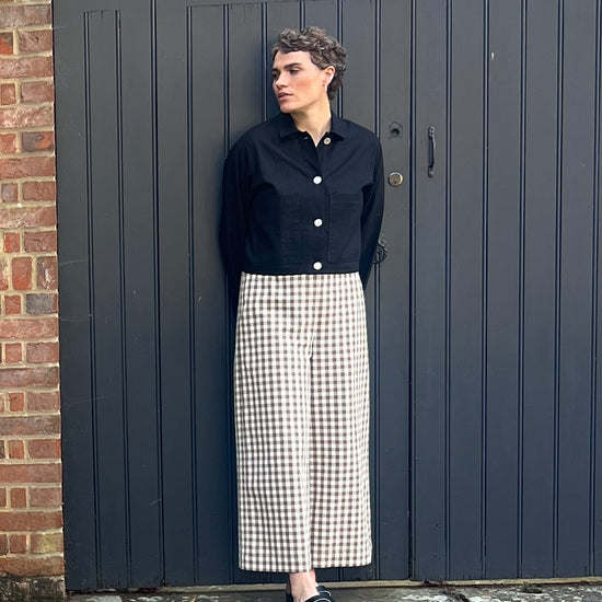 Person wearing a black shirt and white checkered pants standing against a dark gate.