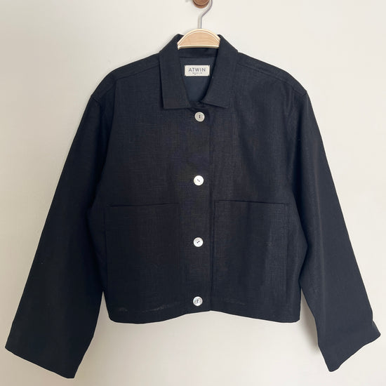 Black workwear jacket on a hanger against a white background