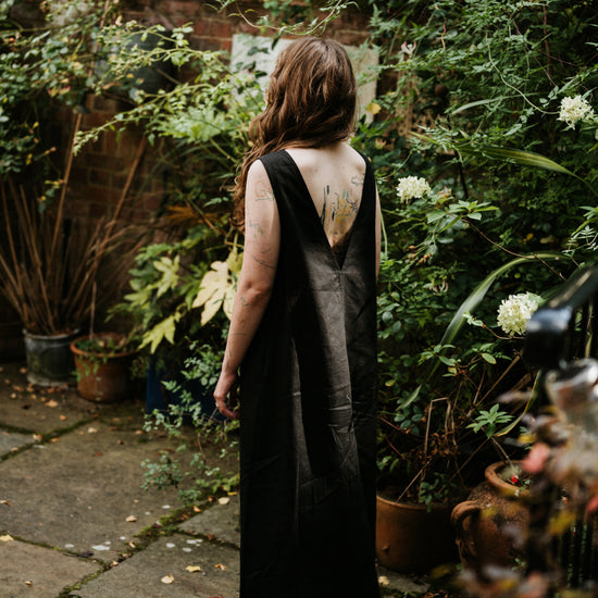 woman standing with her back to us in a low back black linen dress in a garden setting