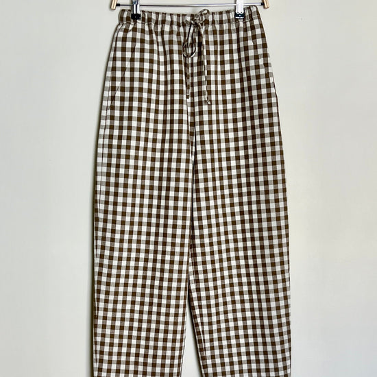 A pair of brown cotton gingham daily trousers with a straight-fit design, high-waisted, with a slim elasticated waistband and drawstring, featuring pockets.