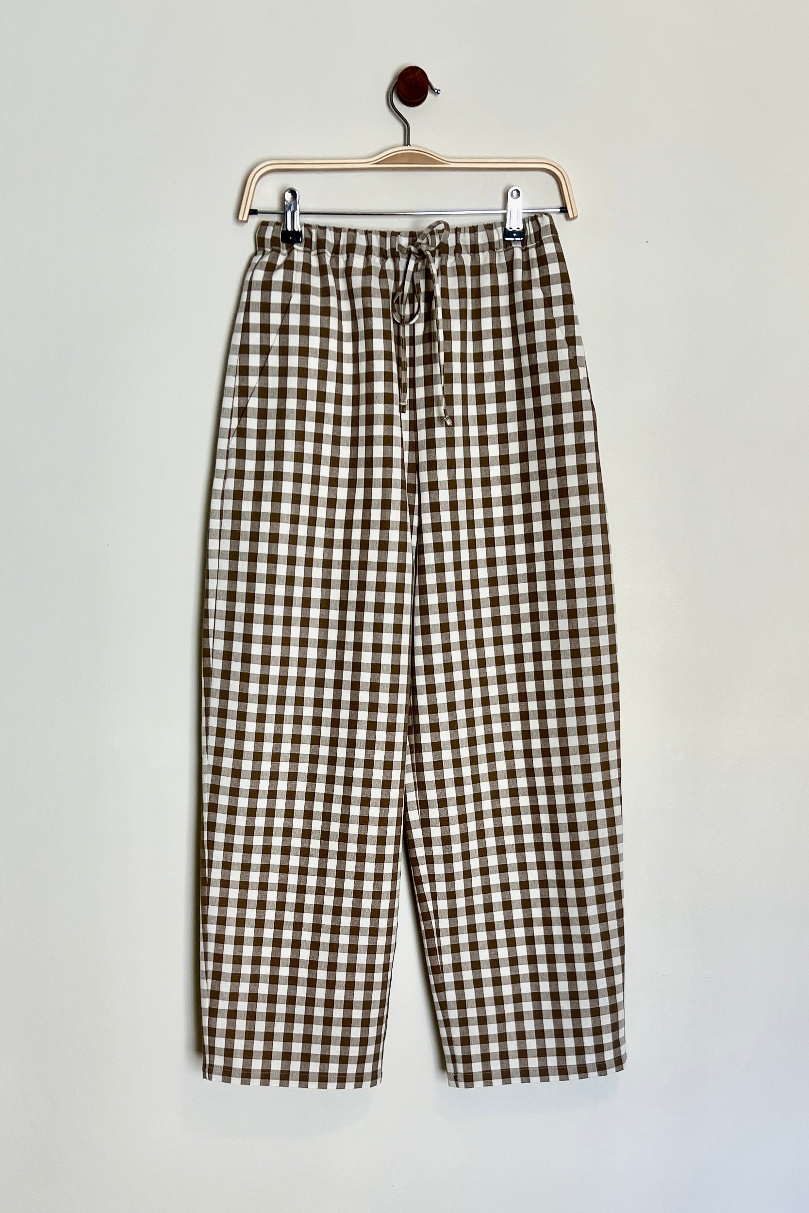 A pair of brown cotton gingham daily trousers with a straight-fit design, high-waisted, with a slim elasticated waistband and drawstring, featuring pockets.