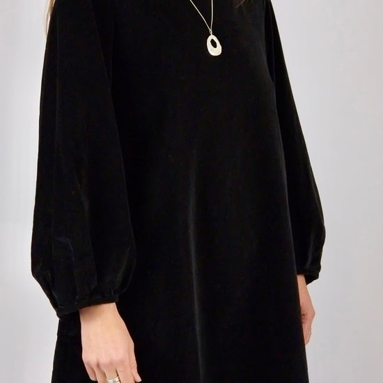 Person wearing a black velvet mini dress handmade by atwin the label with long sleeves on a plain background