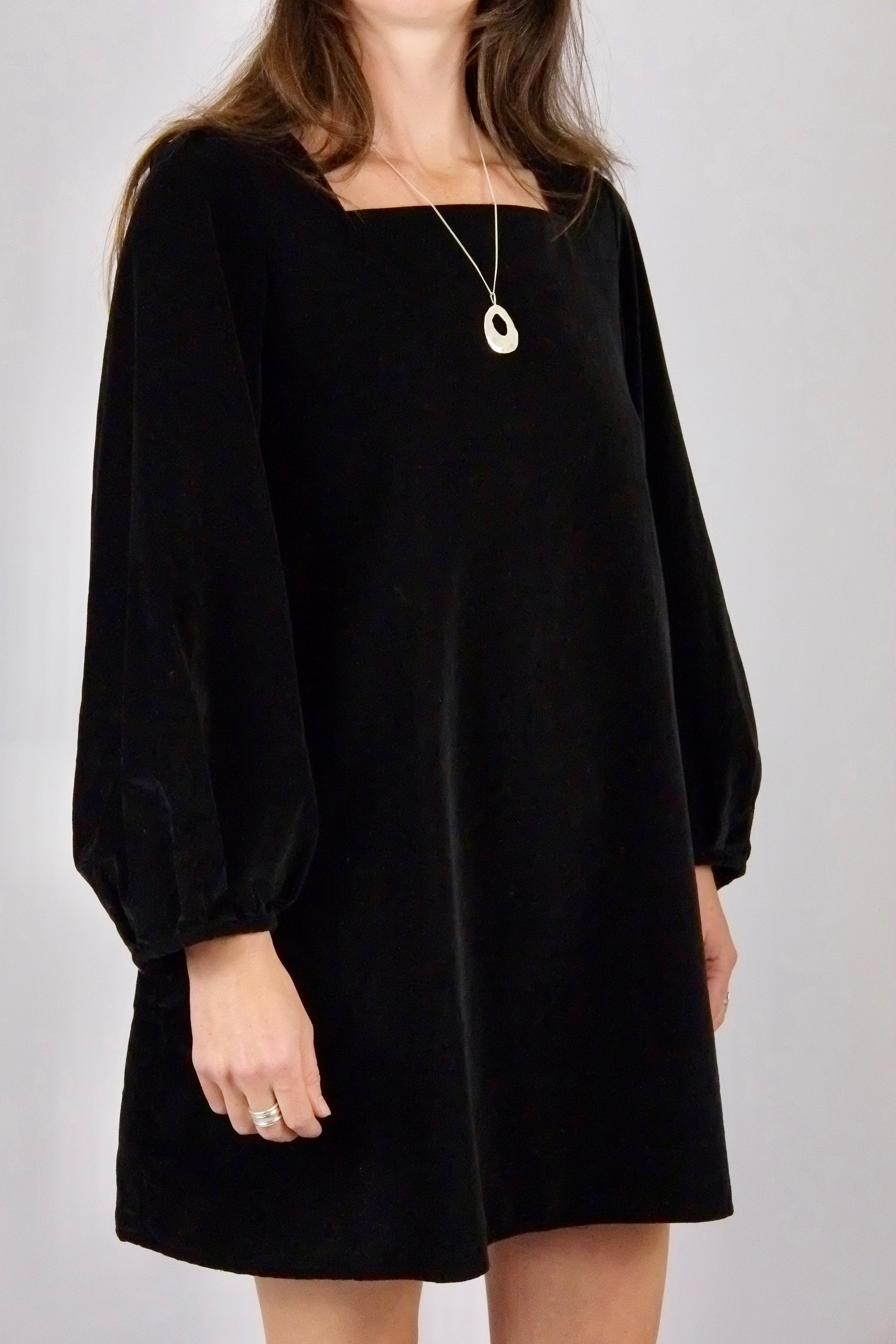 Person wearing a black velvet mini dress handmade by atwin the label with long sleeves on a plain background