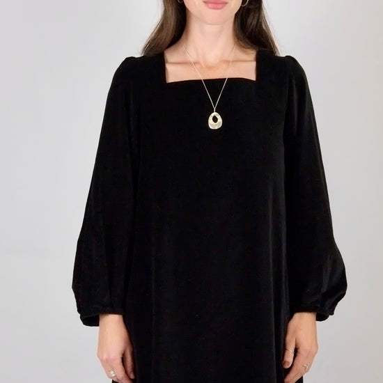 Woman wearing a black velvet mini  dress with long sleeves on a plain background