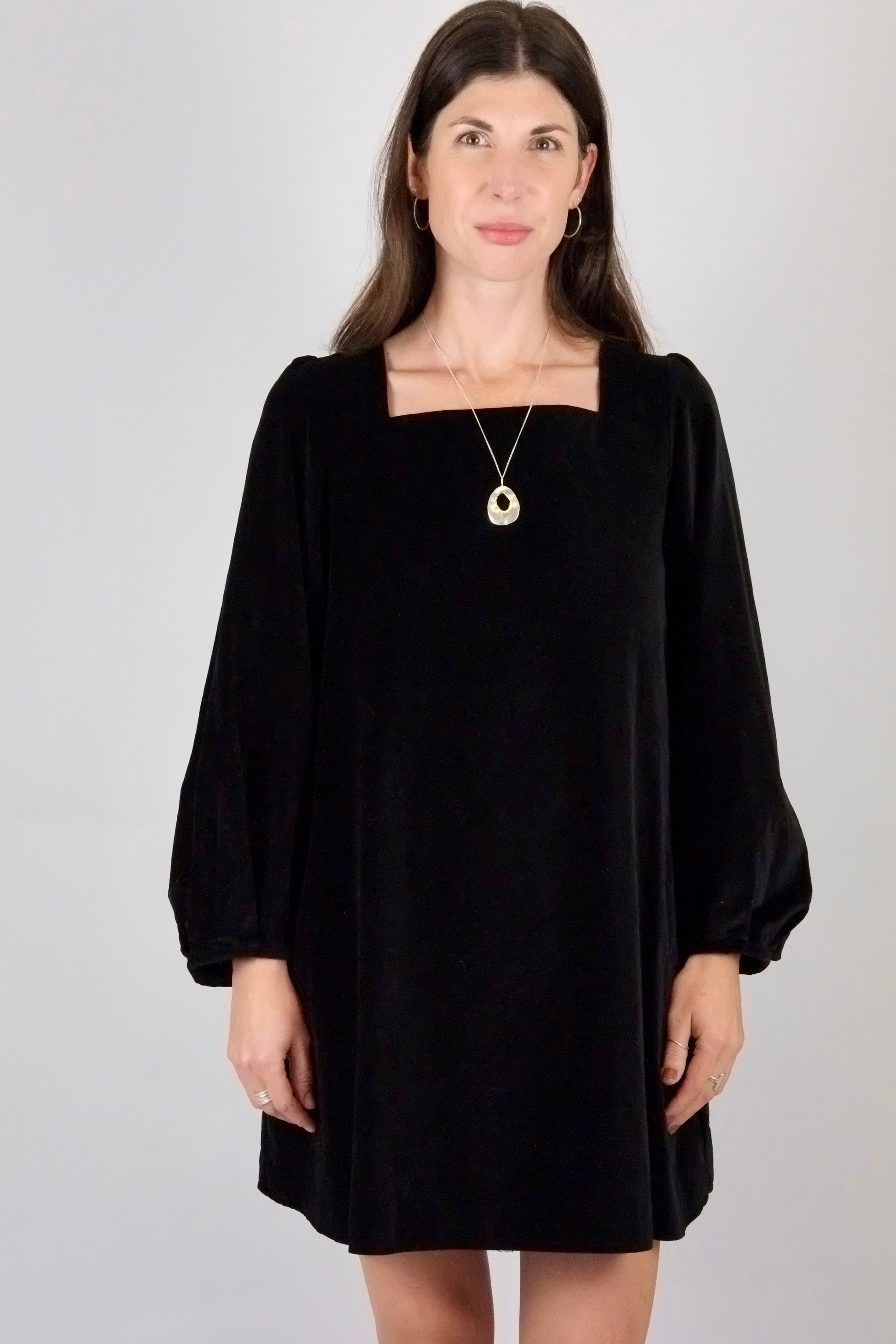Woman wearing a black velvet mini  dress with long sleeves on a plain background