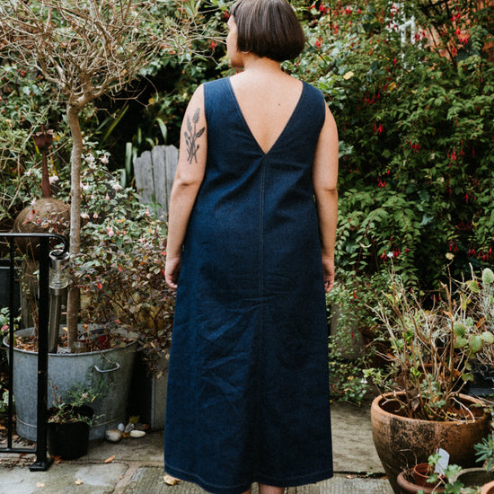 Person wearing an indigo denim blue dress standing in a garden with plants and a house in the background