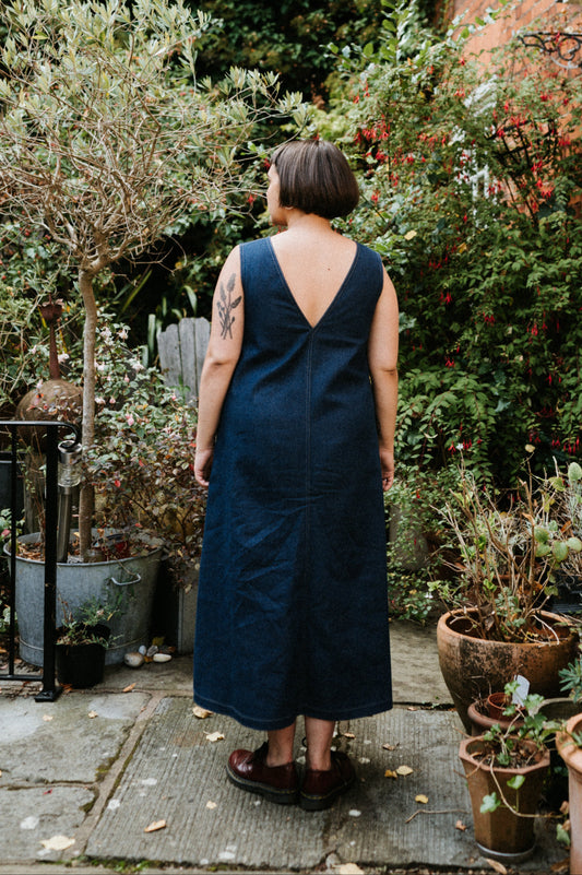 Person wearing an indigo denim blue dress standing in a garden with plants and a house in the background