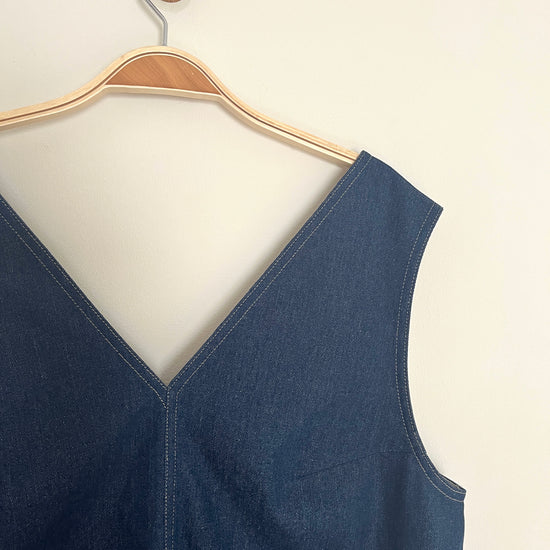 Blue sleeveless overall denim dress on a hanger against a white background