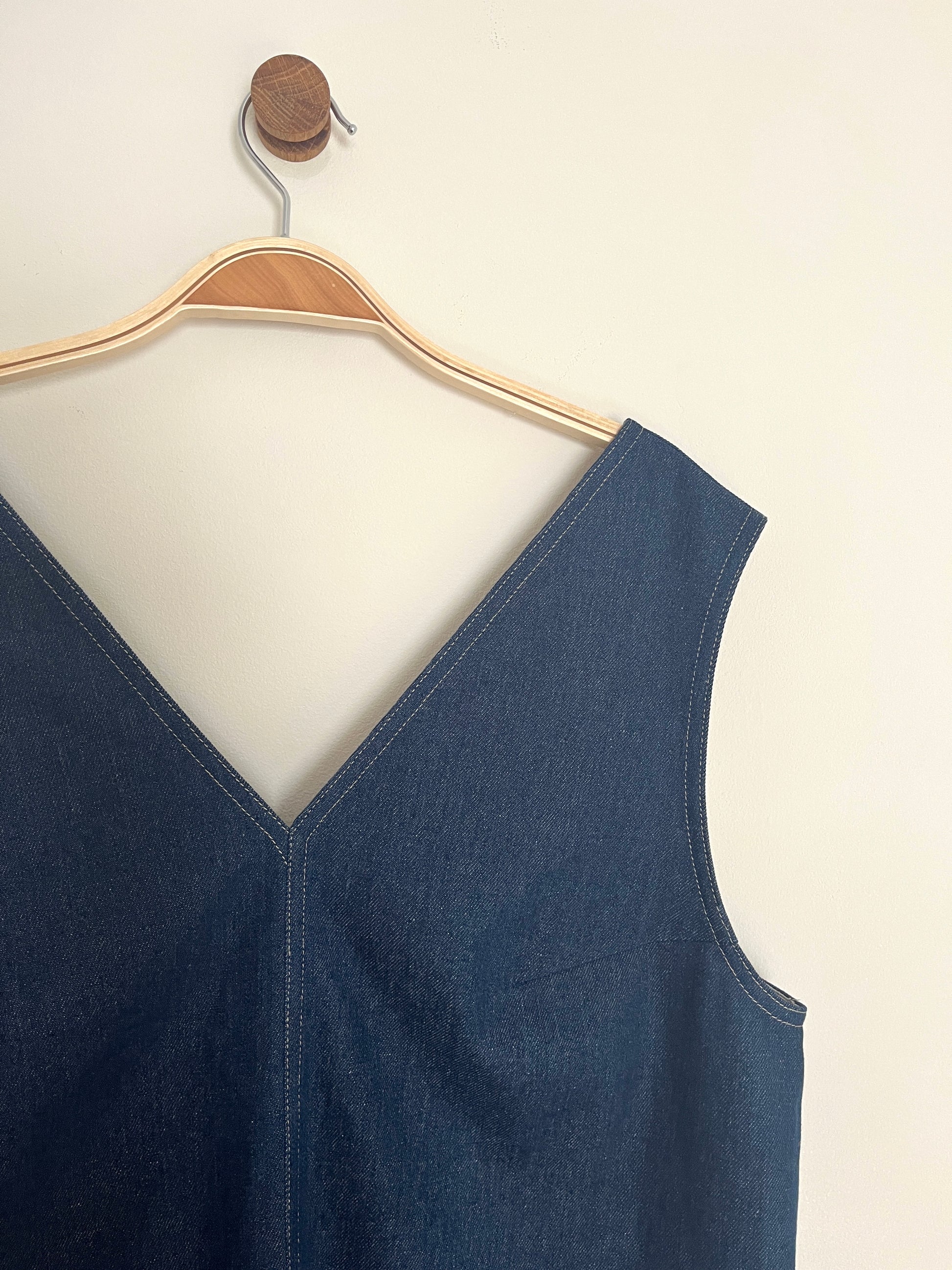 Blue sleeveless overall denim dress on a hanger against a white background