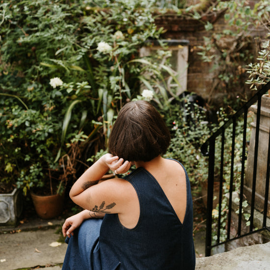 Person sitting on a stone wall in a garden with greenery and a house in the background