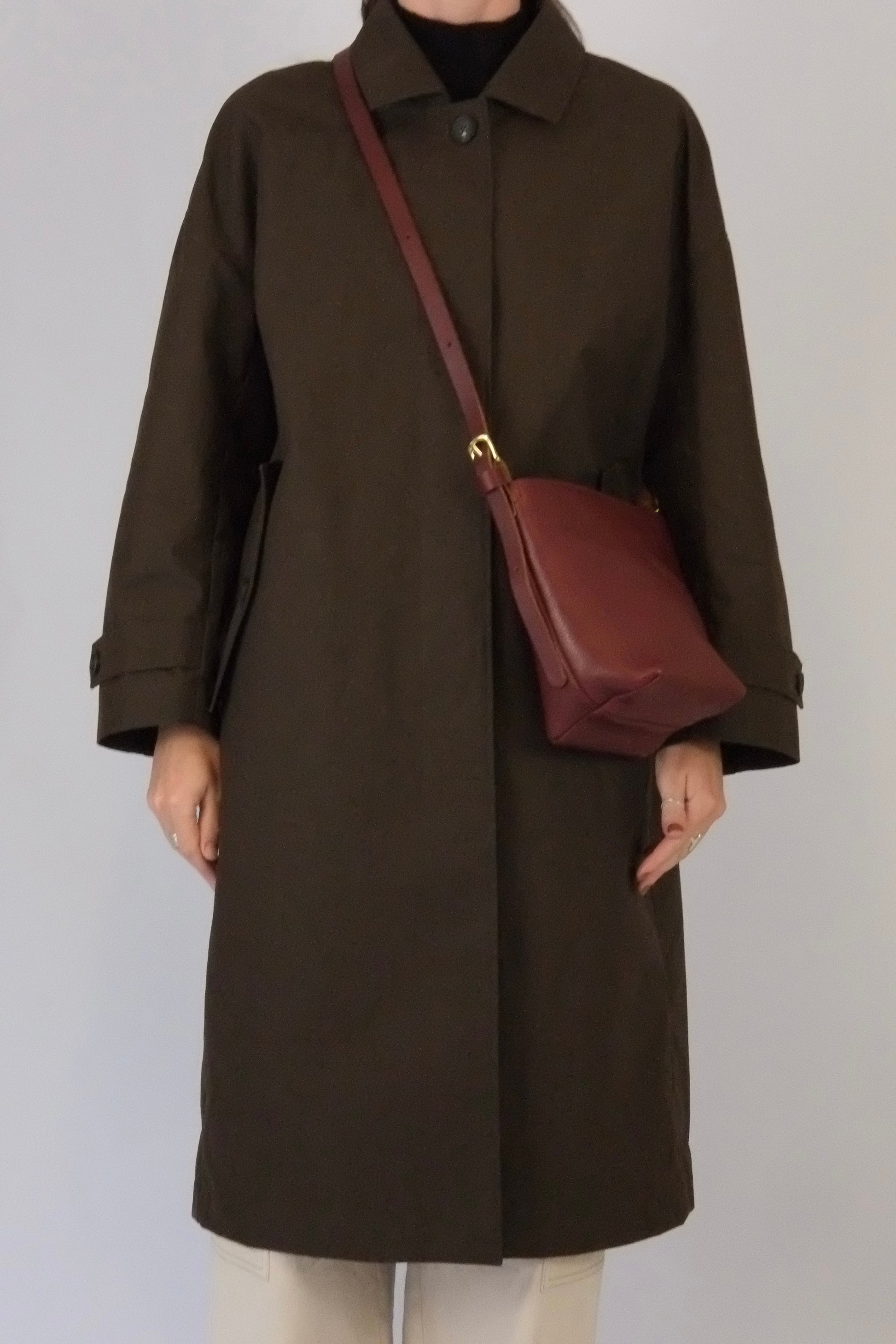 Person wearing a brown coat with a maroon bag on a plain background