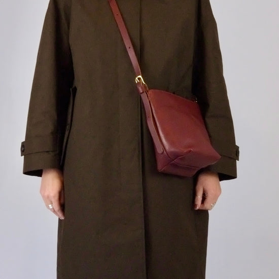 Person wearing a brown coat with a red bag and patterned scarf on a plain background