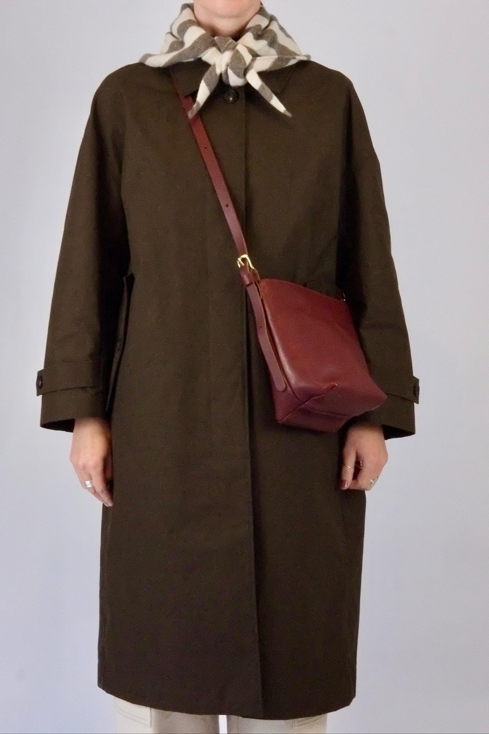 Person wearing a brown coat with a red bag and patterned scarf on a plain background