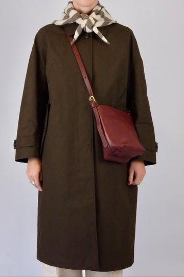 Person wearing a brown coat with a red bag and patterned scarf on a plain background