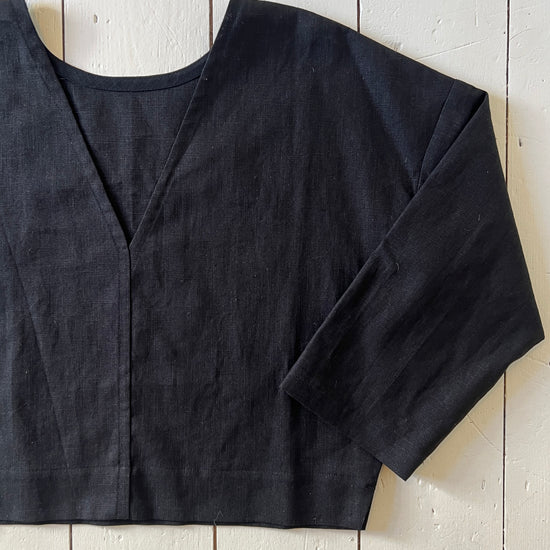 A black reversible top with a deep v-neck on one side and a high scoop neck on the other, laid flat on a wooden surface.