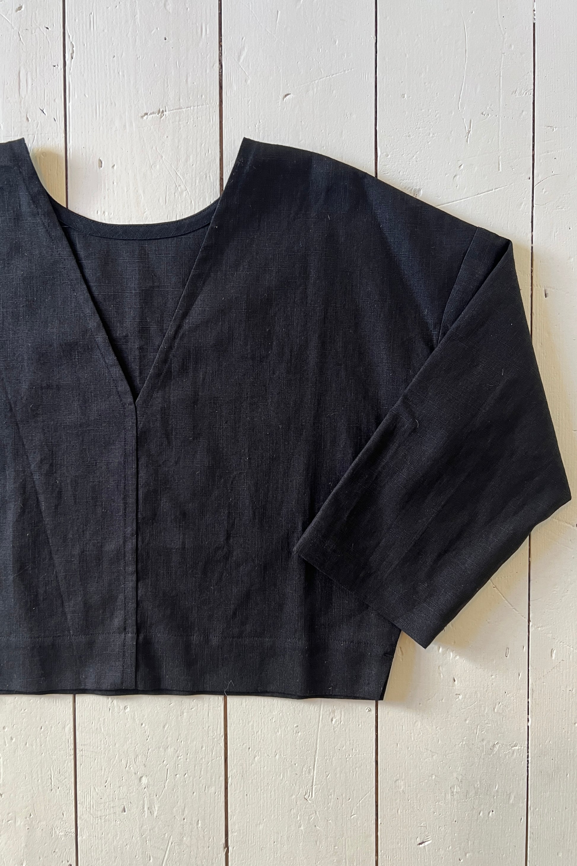 A black reversible top with a deep v-neck on one side and a high scoop neck on the other, laid flat on a wooden surface.