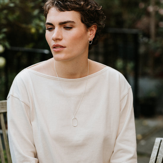 Woman wearing a white smock sweater sitting outdoors with a blurred background