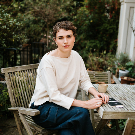 Person sitting at a wooden table outdoors with greenery in the background