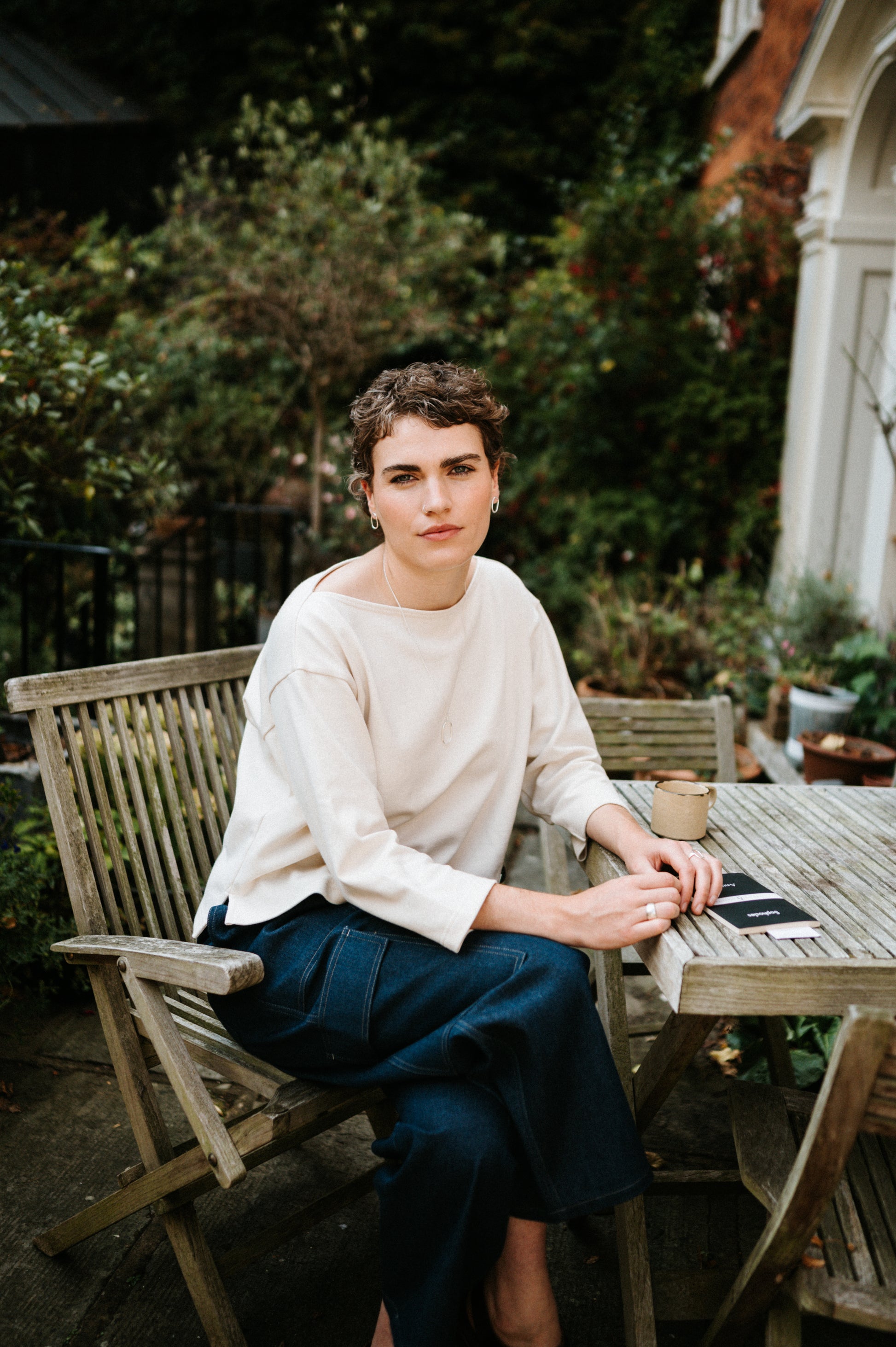 Person sitting at a wooden table outdoors with greenery in the background