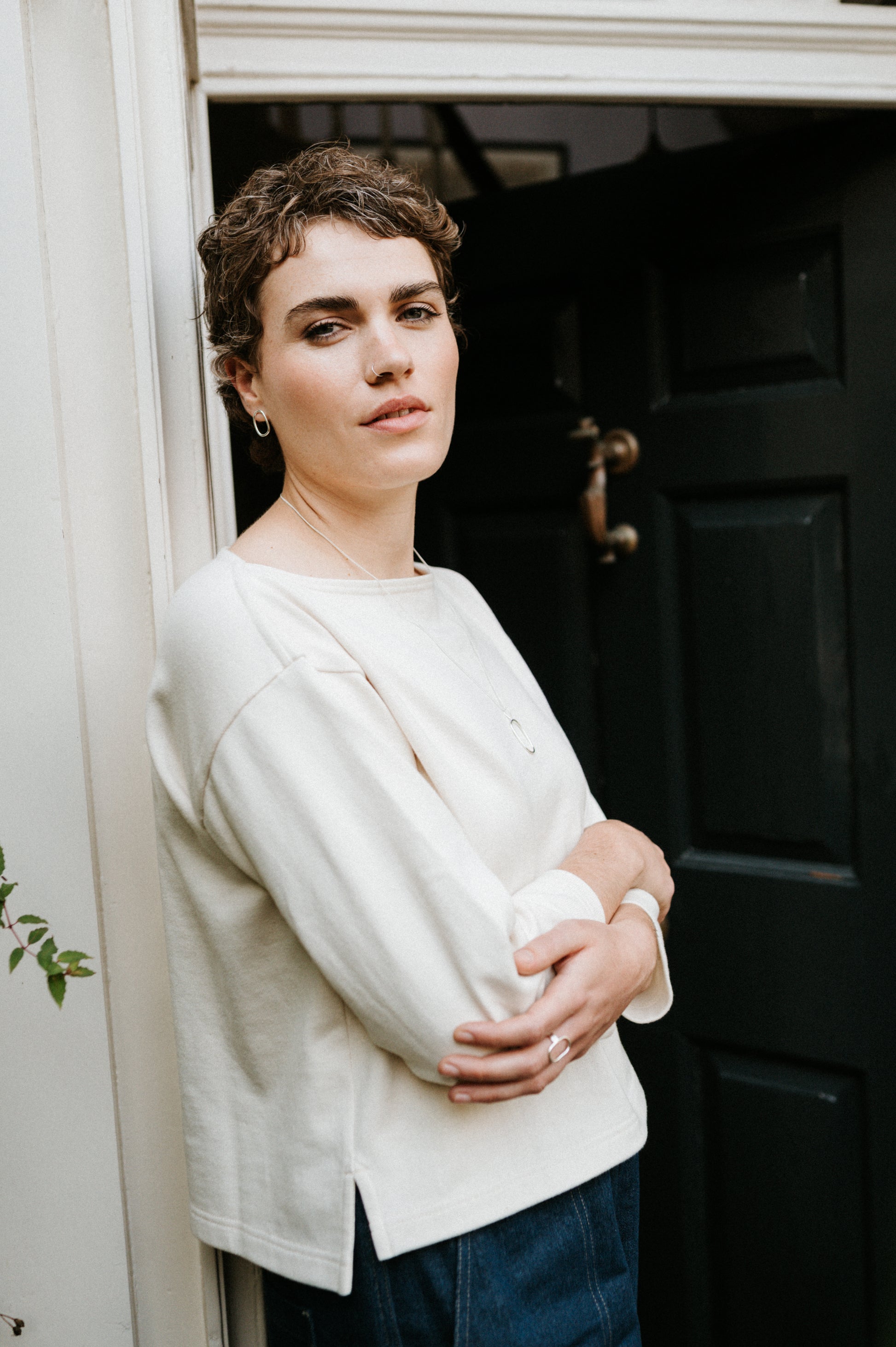 Woman standing in a doorway wearing a ecru smock top and blue jeans.