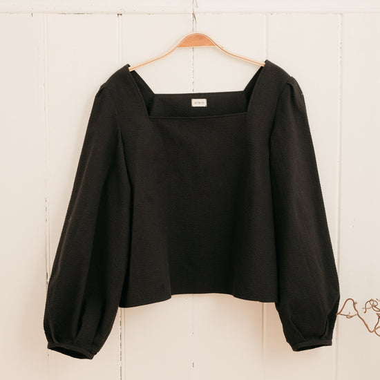 handmade seersucker blouse in black hanging on a hook against a wall