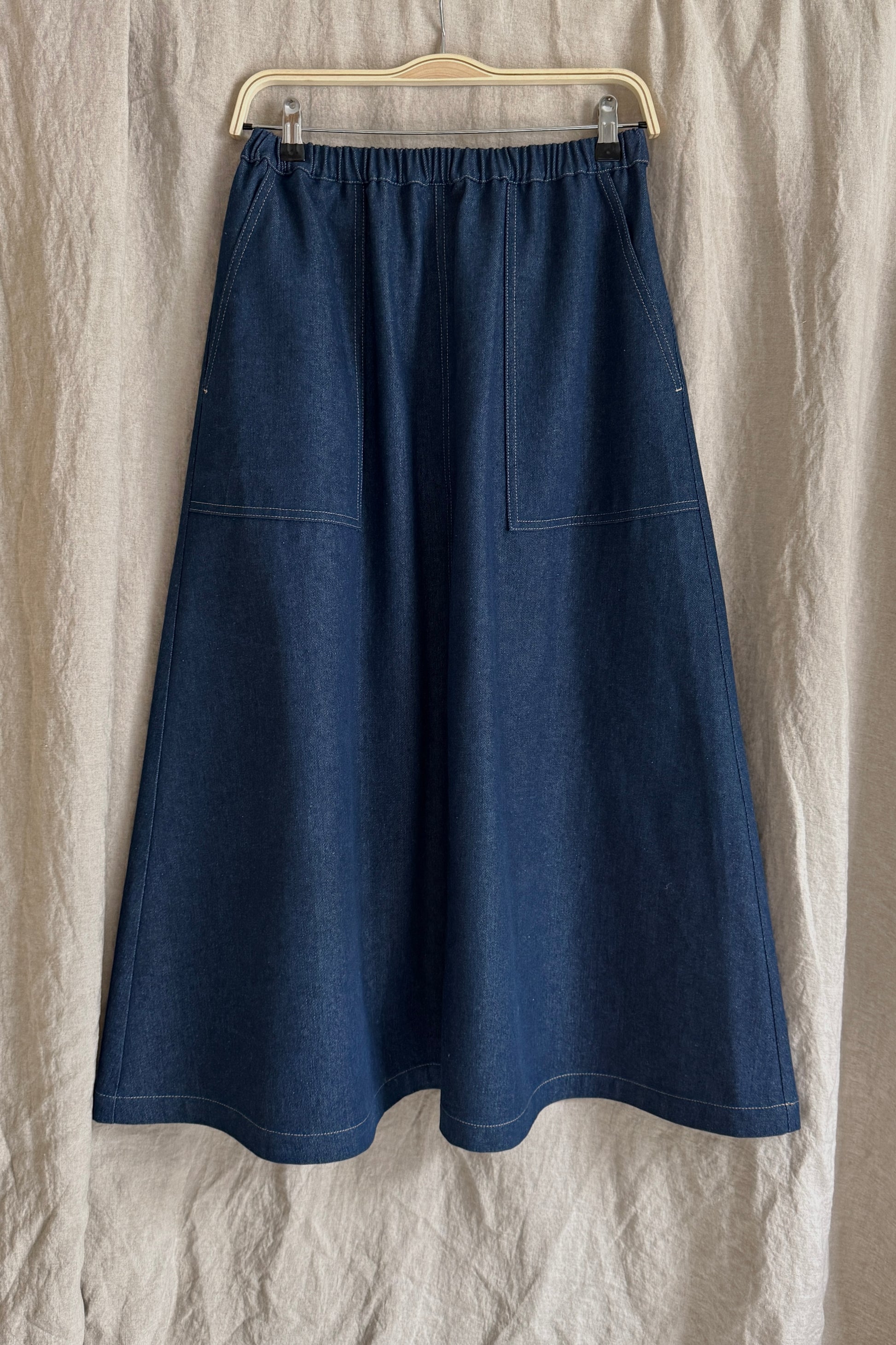 Blue denim skirt on a hanger against a beige fabric background