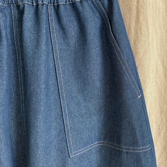 Blue denim skirt hanging on a wooden hanger against a beige background