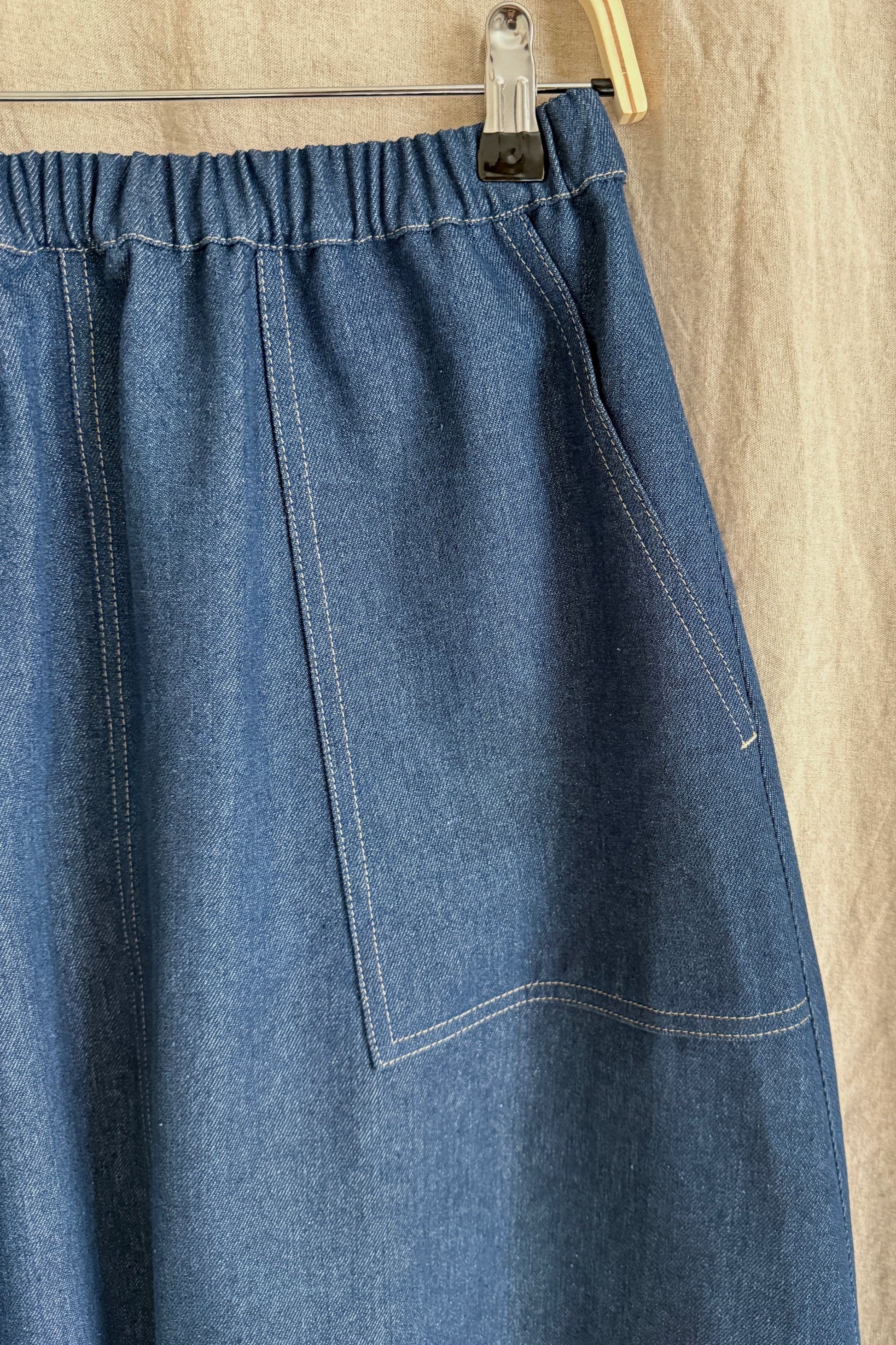 Blue denim skirt hanging on a wooden hanger against a beige background