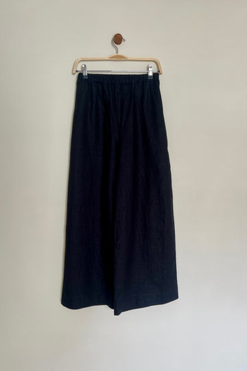 A pair of high-waisted, wide leg trousers in a paprika color, made from linen, displayed on a hanger against a neutral background.