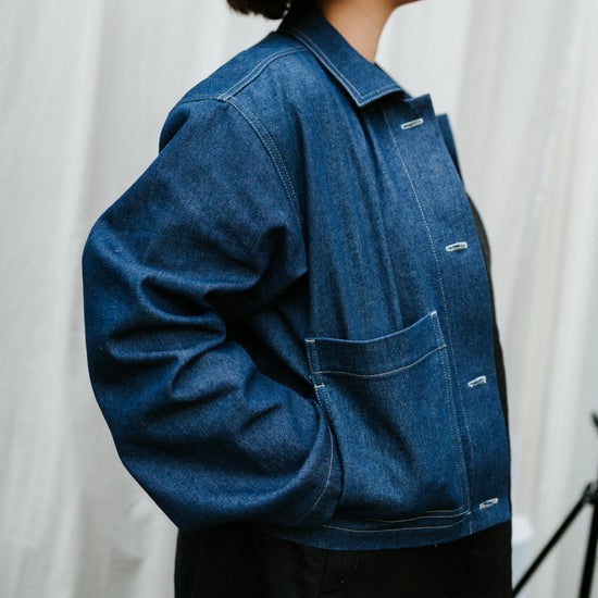 Person wearing a blue denim jacket against a white curtain background