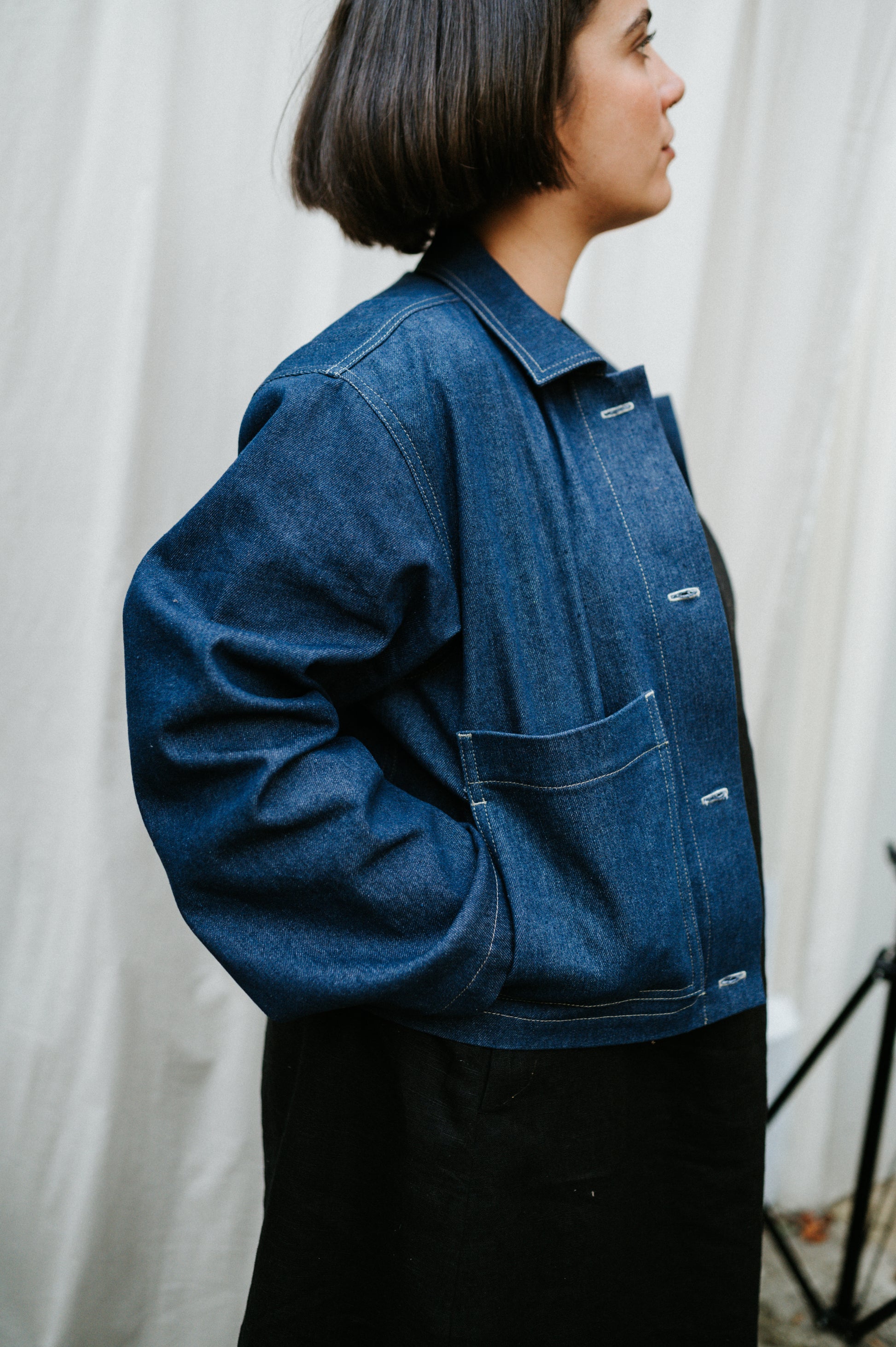 Person wearing a blue denim jacket against a white curtain background