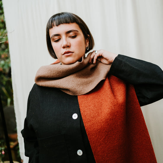 Person wearing a black coat with a red scarf against a white curtain background