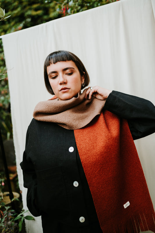Person wearing a black coat with a red scarf against a white curtain background