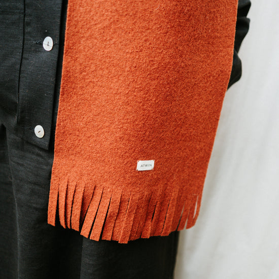 Orange scarf with a brand label draped over a black garment on a white background