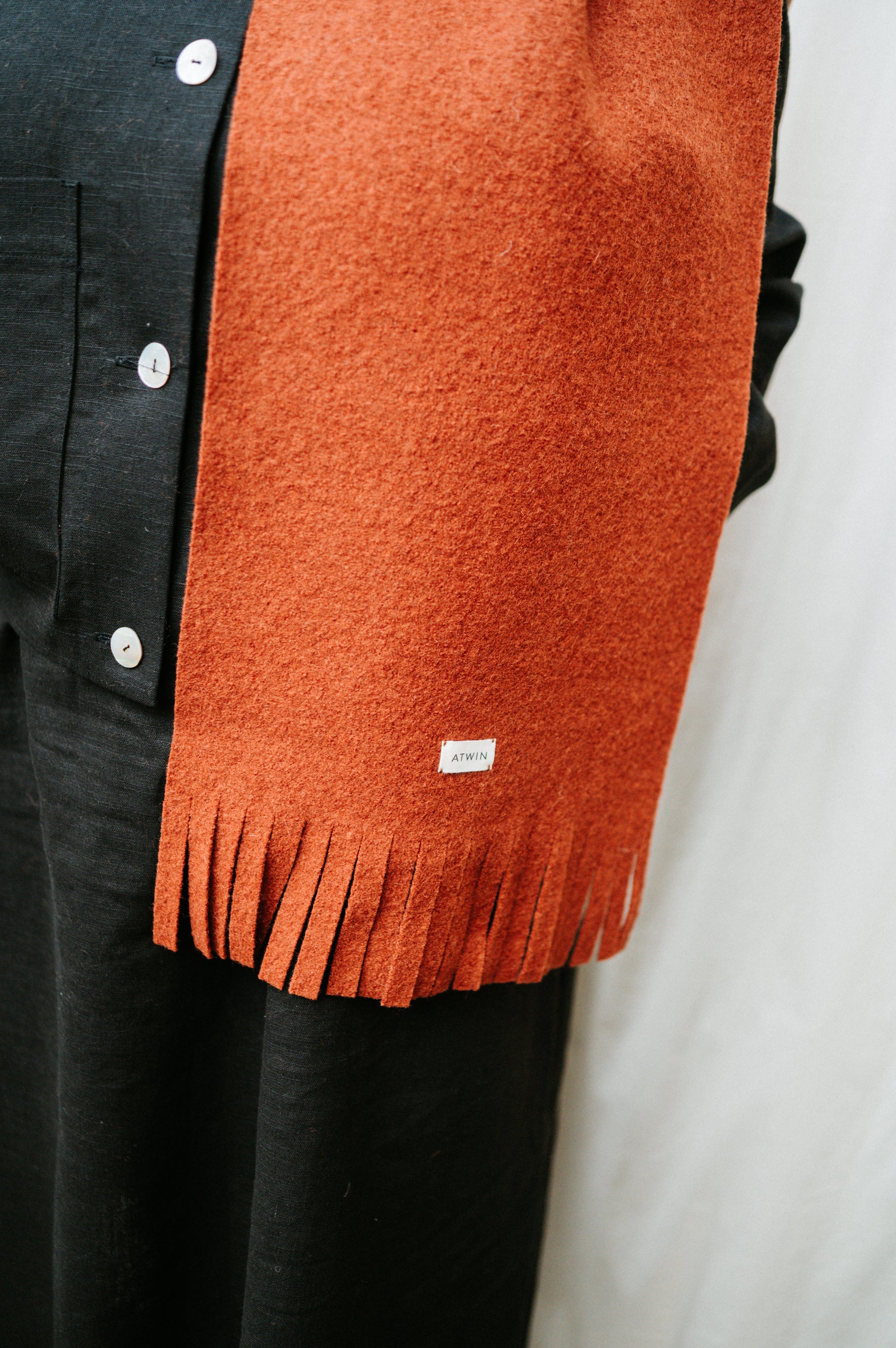 Orange scarf with a brand label draped over a black garment on a white background
