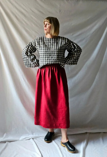 Woman wearing a black and white checkered top and red skirt against a plain background