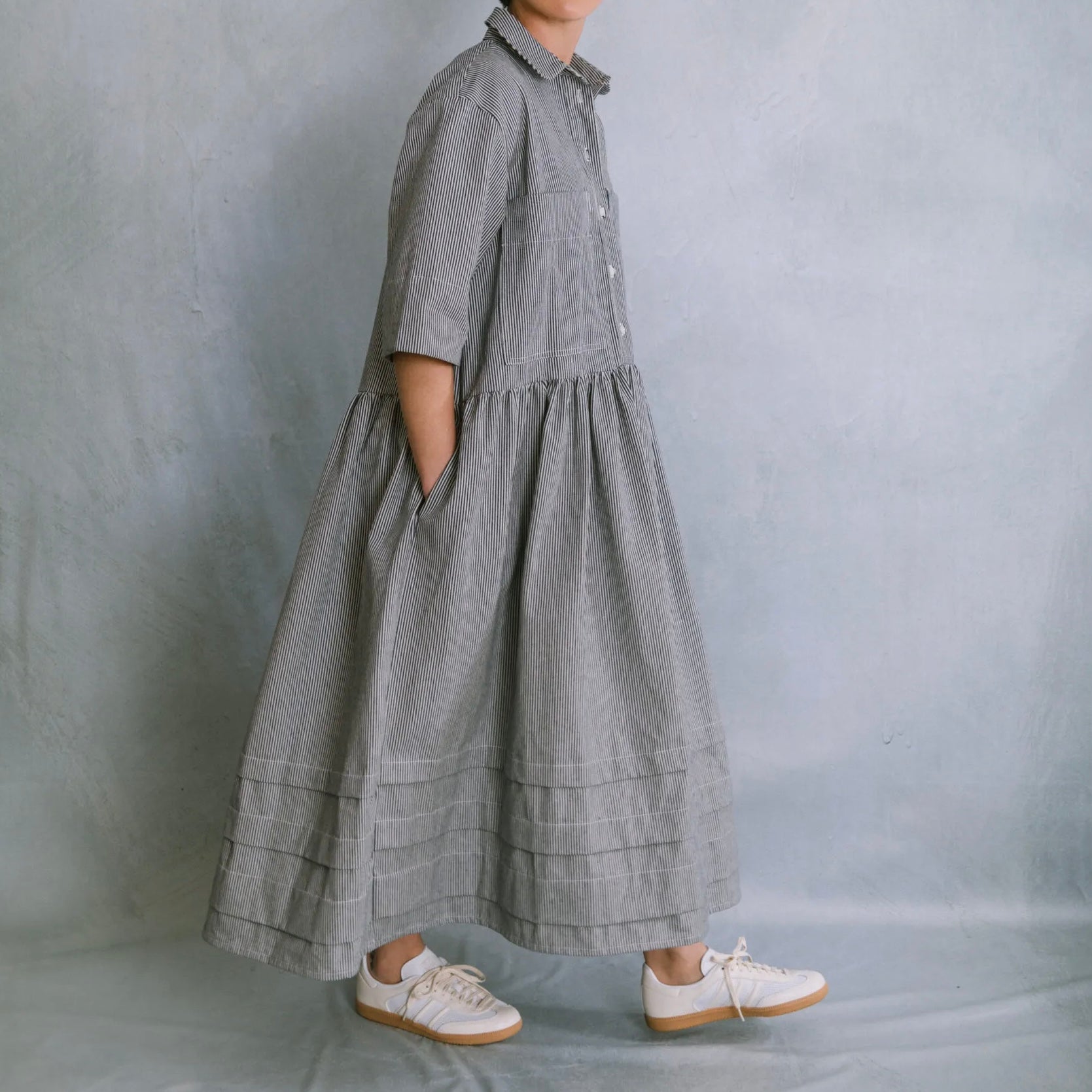 Person wearing a long gray dress with a plain background