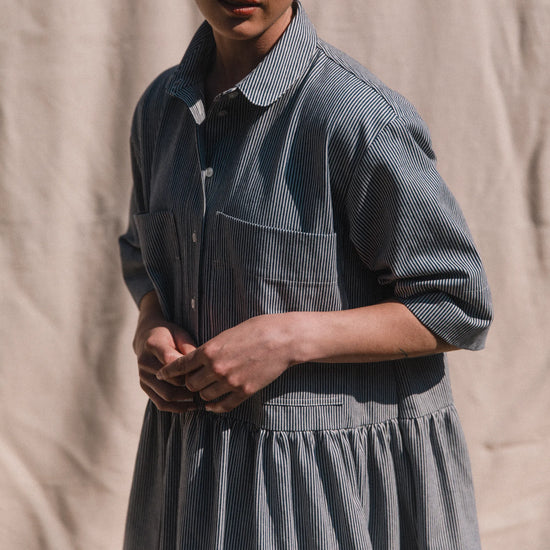 Person wearing a blue striped dress against a beige background