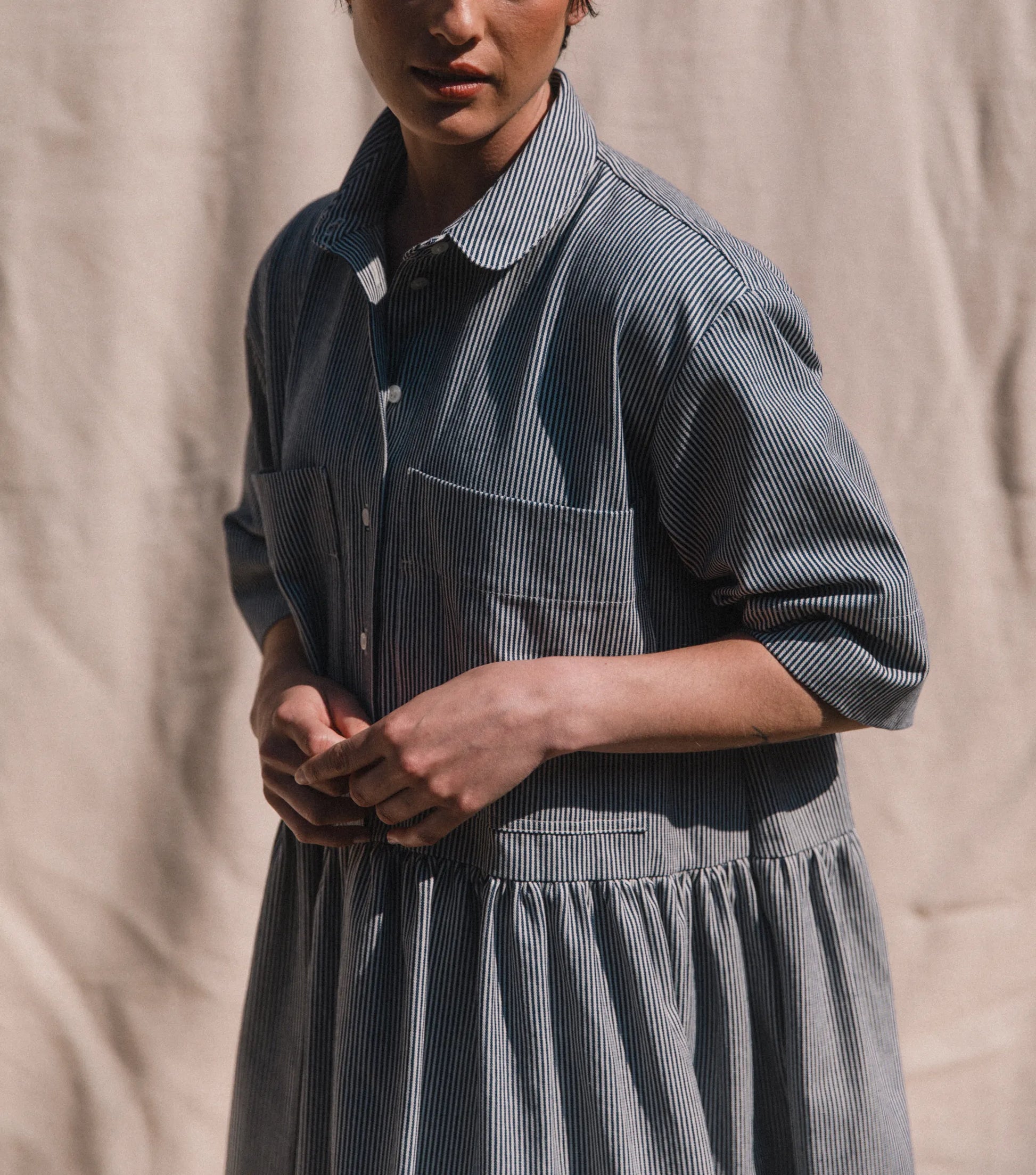 Person wearing a blue striped dress against a beige background